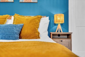 A bed with yellow and blue pillows, a bedside lamp, and a wooden nightstand. - 3Bedroom Sleeps 5 at Buxton (Buxton)