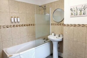 Un baño con bañera, lavamanos y ducha. Hay tres botellas en la pared.