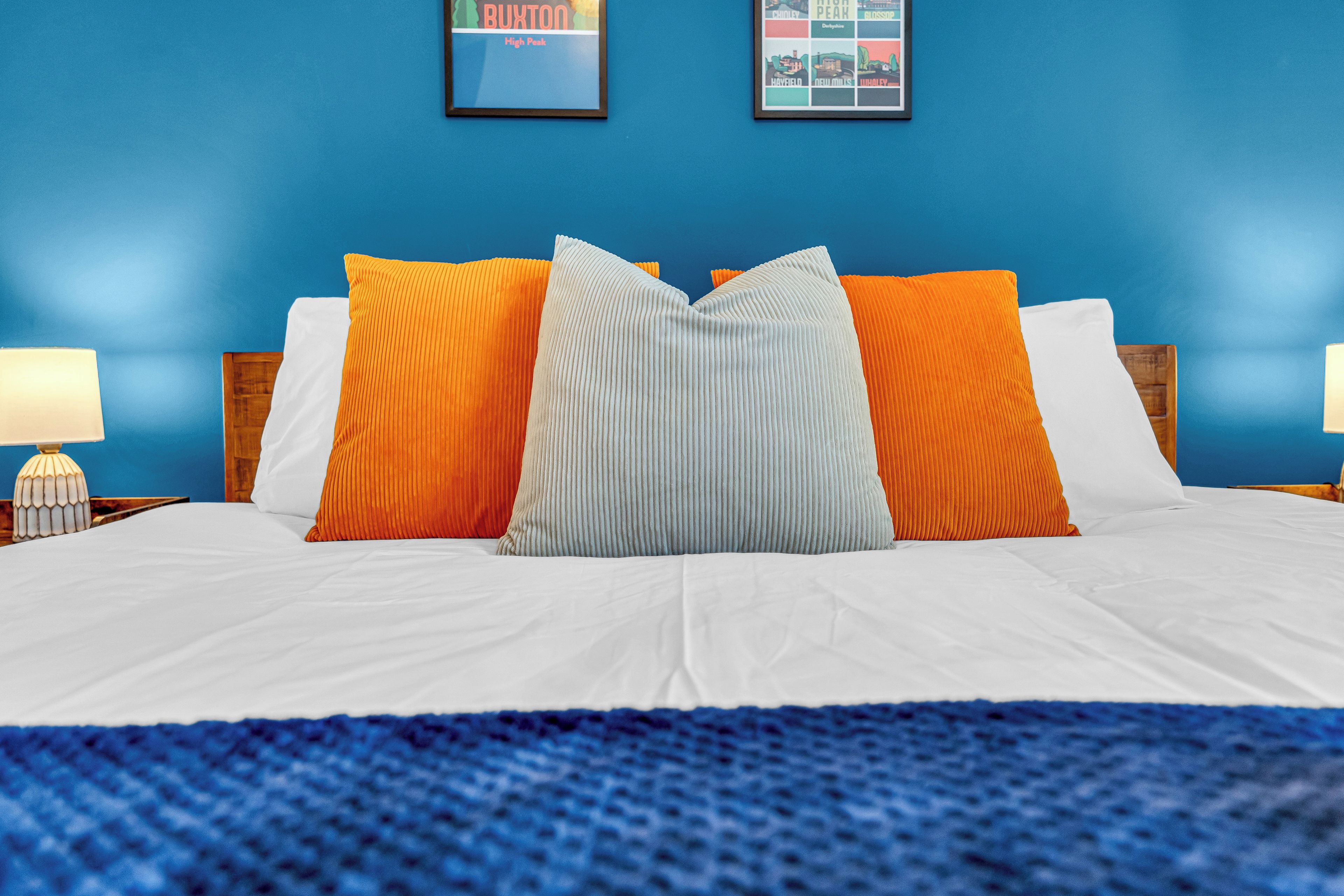 A bed with white bedding and multiple pillows in orange and gray colors.
