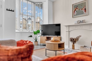 Ein modernes Wohnzimmer mit Fernseher, Kamin und einem großen Fenster mit Jalousien.