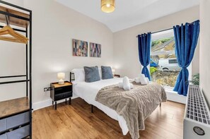 Un dormitorio con cama, mesita de noche y ventana con cortinas.