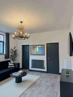 A modern living room with a black sofa, a coffee table, a chandelier, and a fireplace. - New Cosy Retreat in Matlock Bath (Matlock Bath)