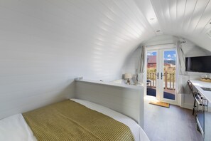 Ein Schlafzimmer mit Bett, Schreibtisch mit Stuhl, Fenster mit Vorhängen und Blick ins Freie.