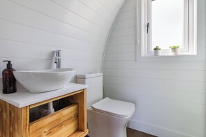 Ein Badezimmer mit einem weißen Waschbecken, einem Holz-Waschtisch, einer weißen Toilette und einem Fenster mit Pflanzen.