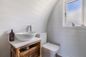 Ein Badezimmer mit einem weißen Waschtisch, einer Toilette und einem Fenster mit Blick auf den Himmel.