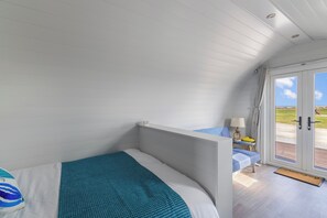 Ein Schlafzimmer mit einem Bett, einem kleinen Tisch mit Lampe und Blick ins Freie durch eine Tür.