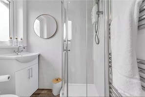 Een moderne badkamer met een glazen douchecabine, een ronde spiegel, een witte wastafel en een toilet.