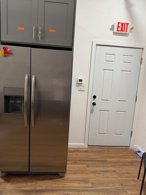 Un refrigerador de acero inoxidable con un compartimento congelador, una puerta blanca con manija, y una señal de salida arriba.