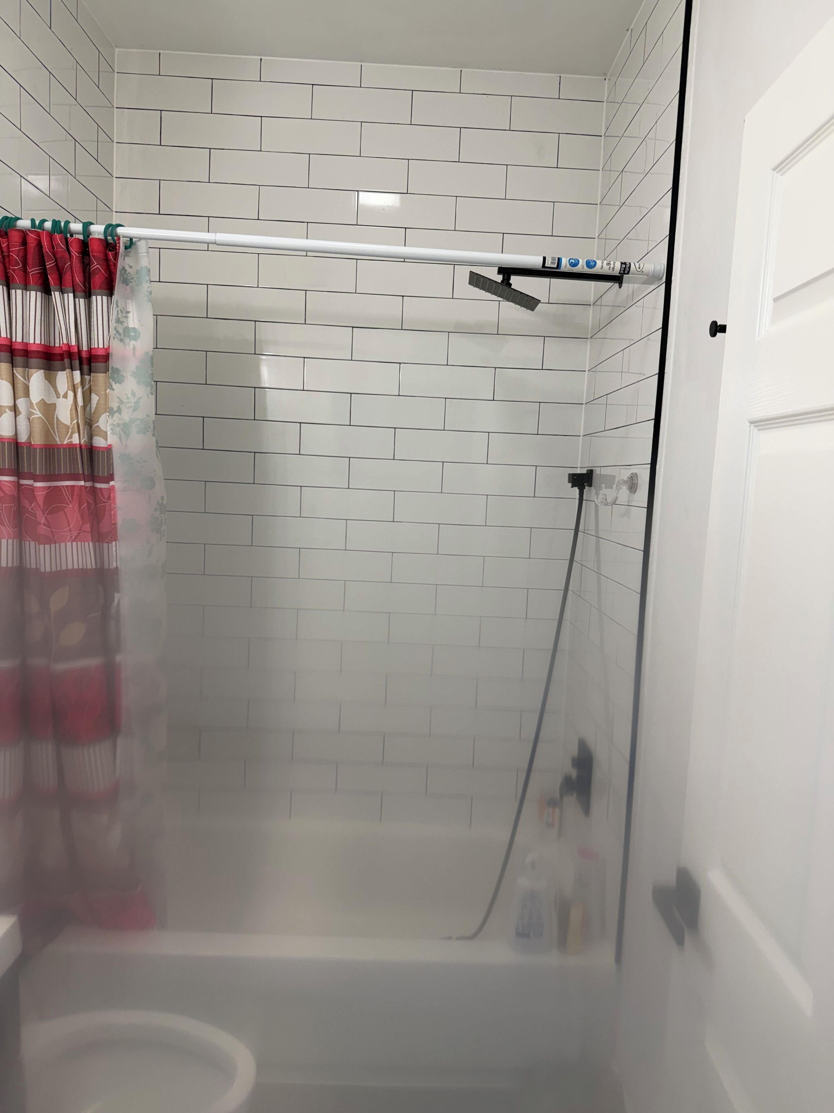 A shower area with a glass door, white tiled walls, and a showerhead.