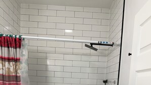 Un angolo doccia con porta in vetro, pareti rivestite di piastrelle bianche e soffione.