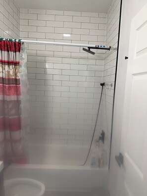 Zona de ducha con puerta de vidrio, paredes de azulejos blancos y ducha.