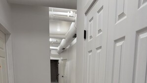 Un corridoio con porte bianche e pavimento in legno, che conduce a una stanza con cabina doccia.