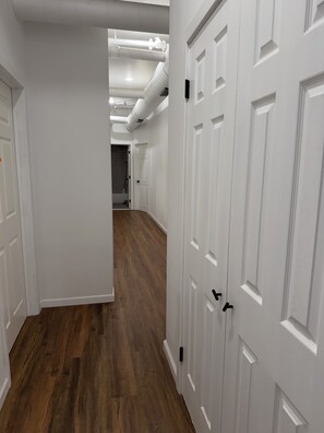 Un pasillo con puertas blancas y piso de madera, que conduce a una habitación con zona de ducha visible.