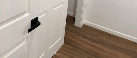 A white door with a black handle, leading to a hallway with wooden flooring.