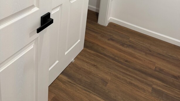 Una porta bianca con maniglia nera, che dà su un corridoio con pavimento in legno.