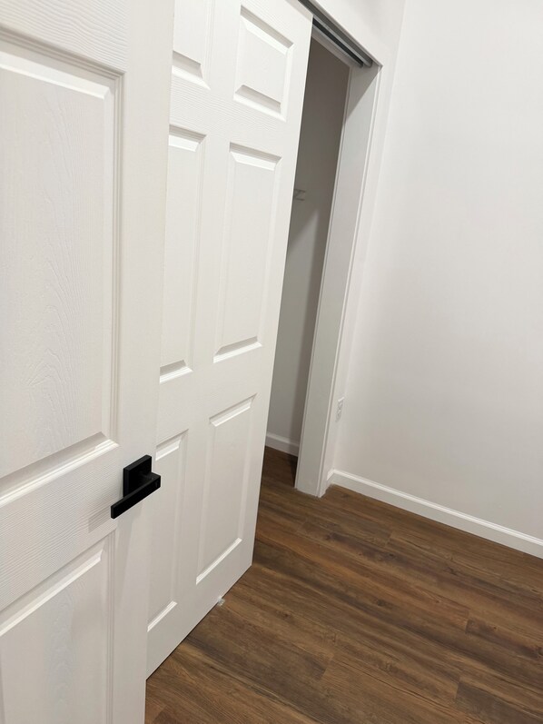 Puerta blanca con pomo negro, que da a un pasillo con suelo de madera.