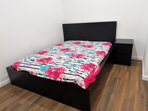Ein Bett mit schwarzem Gestell, einer blumigen Tagesdecke und einem passenden Nachttisch.