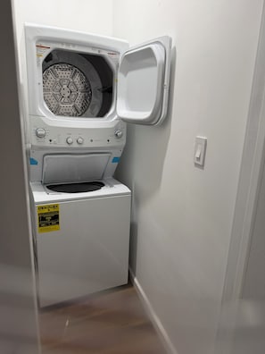 A compact, white front-loading washing machine in a small laundry room with a door. - Terrific 3-bedroom apartment with AC in vibrant Philadelphia’s Center City (Philadelphia)
