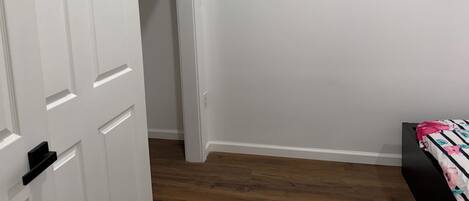 A room with a wooden floor, a bed with a floral bedspread, and a white door leading to a closet.