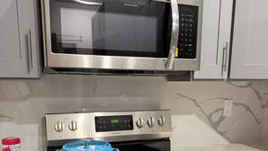 Una cucina con un forno a microonde in acciaio inox, un forno con orologio digitale e una pentola blu sul fornello.