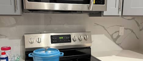 A kitchen with a stainless steel microwave, an oven with a digital clock, and a blue pot on the stovetop.