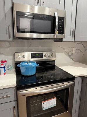 Una cocina con un microondas de acero inoxidable, un horno con reloj digital y una olla azul sobre la estufa.