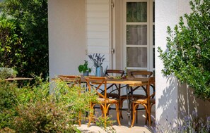Eine Terrasse im Freien mit Tisch und Stühlen, umgeben von viel Grün.