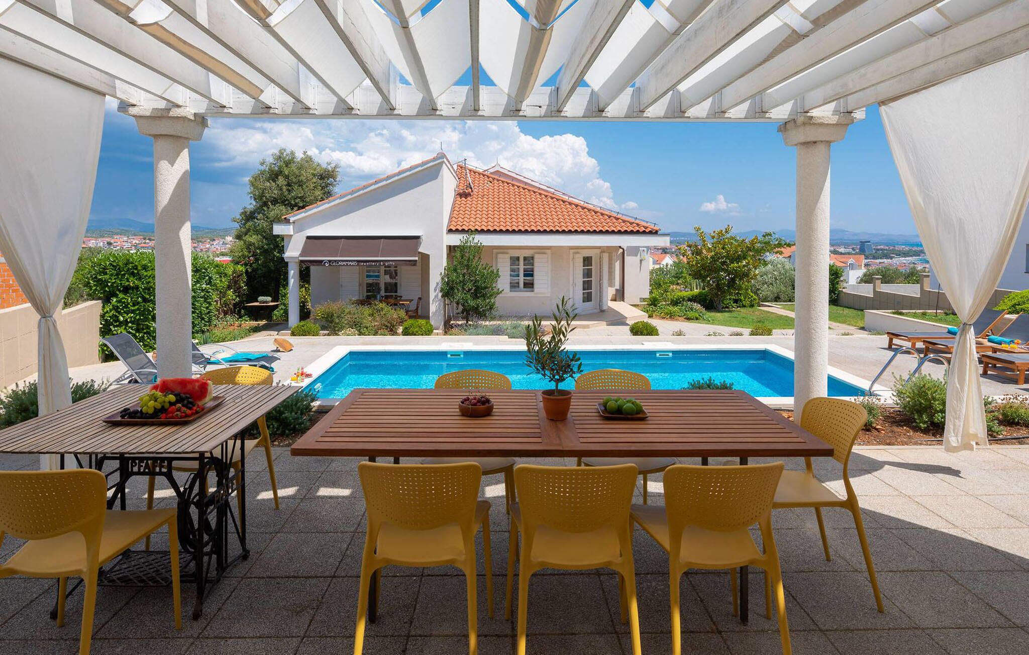 An outdoor patio with a pool, yellow chairs, and a table with fruit.