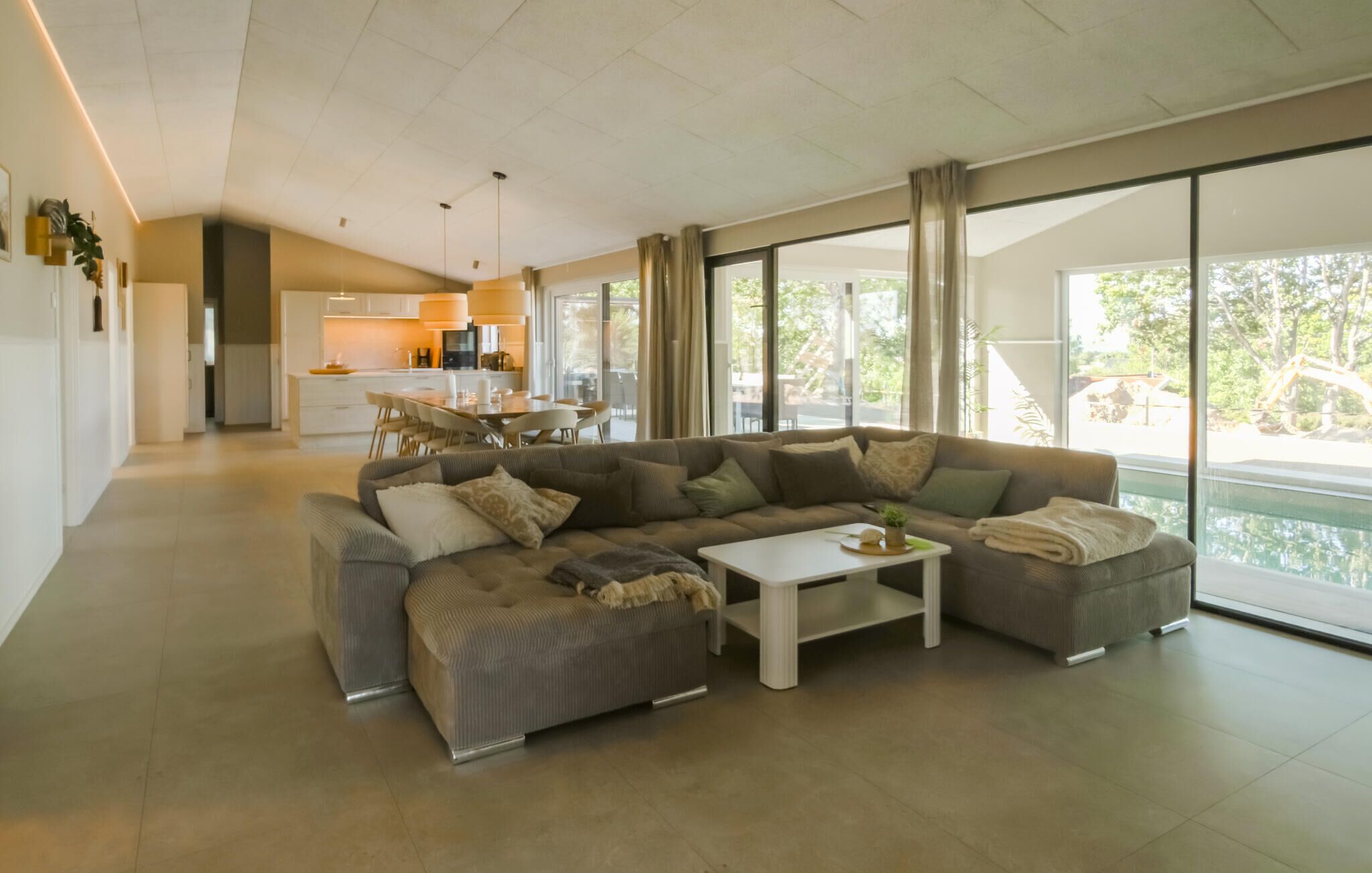 A modern living room with a sectional sofa, a coffee table, and a view of the outdoors through large windows.