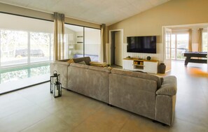 A modern living room with a large striped sofa, a flat-screen TV, and a pool view. - Luxurious home in Ebeltoft with sauna (Ebeltoft)