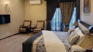 A hotel room with a bed, two chairs, a TV, and a window with curtains.