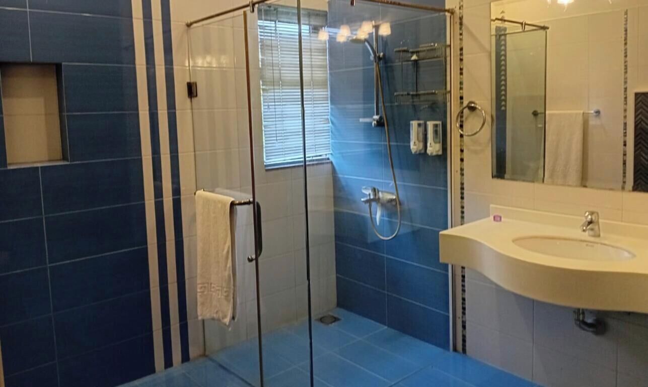 A bathroom with a glass-enclosed shower, a sink with a mirror, and blue-tiled walls.