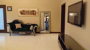 Une pièce avec un canapé vert foncé, un grand miroir, un téléviseur à écran plat et une œuvre d’art encadrée accrochée au mur.