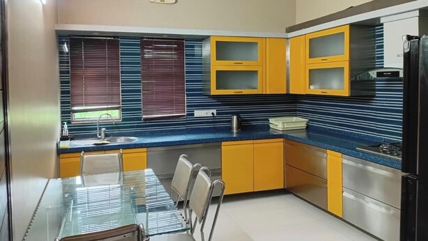 A modern kitchen with yellow cabinets, a blue countertop, and a dining area with a glass table and chairs.