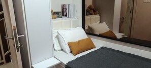 A bedroom with a bed, pillows, a bedside table, a mirror, and a wardrobe. - Guesthouse Puri at Kemang (Jakarta Selatan)
