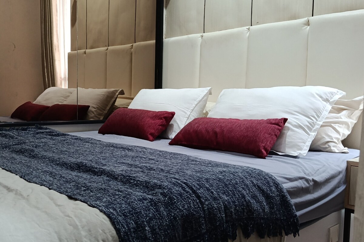 A bed with a headboard, white and red pillows, a dark blue throw blanket, and a wooden headboard.