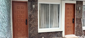 Two wooden doors with square patterns, a window with a white frame, and a wall with a marble-like pattern. - Guesthouse Puri at Kemang (Jakarta)