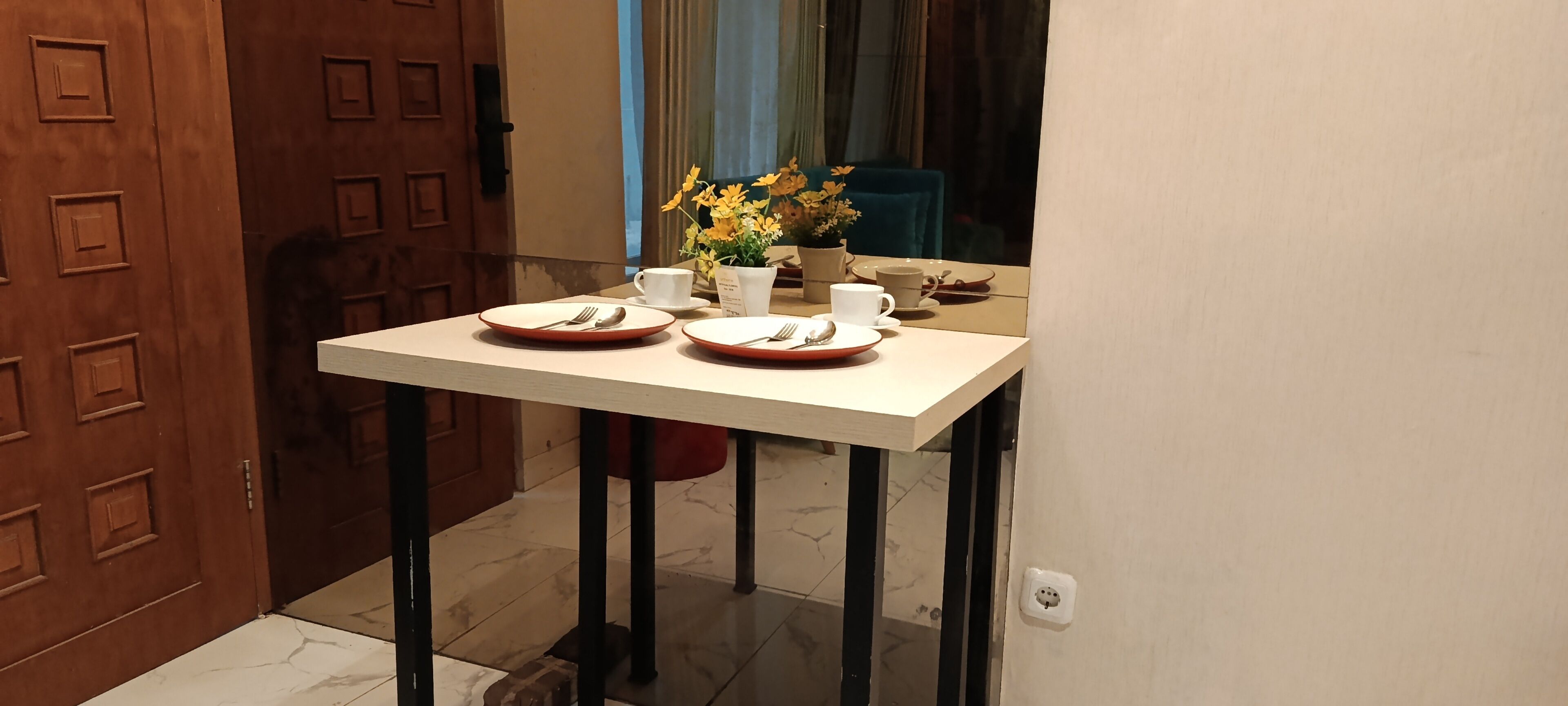 A dining table with two plates, cutlery, and a vase with flowers.