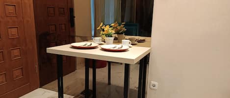 A dining table with two plates, cutlery, and a vase with flowers.