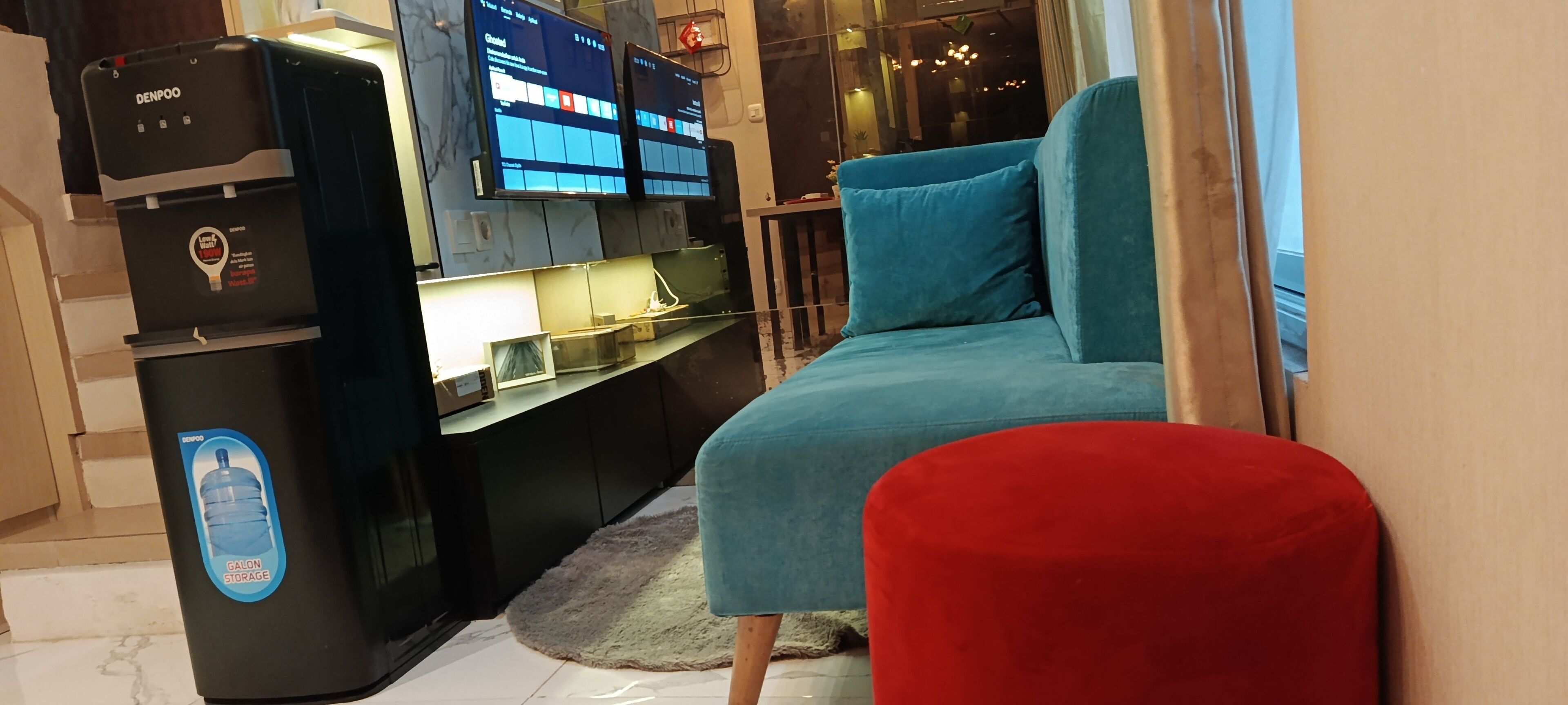 A room with a bed, a red ottoman, a black storage unit, and a wall-mounted TV.