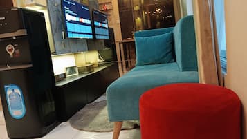 A room with a bed, a red ottoman, a black storage unit, and a wall-mounted TV.