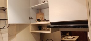 Una cocina con armarios blancos, una campana extractora negra y una pequeña mesa con vajilla.