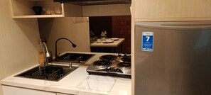 A compact kitchen with a sink, stove, and a refrigerator. - Guesthouse Puri at Kemang (Jakarta Selatan)