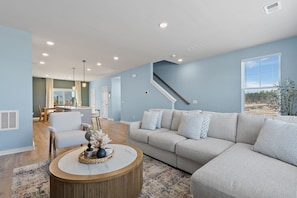 A modern living room with a sofa, coffee table, and a view of the kitchen and staircase. - Cane Bay / Summerville getaway—where Southern hospitality meets modern comfort. (Summerville)