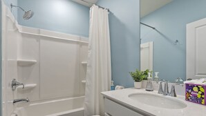 Et badeværelse med badekar, toilet, vask og en bruser med gardin.