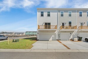 A multi-story residential building with a garage, a small lawn, and a clear sky. - Cane Bay / Summerville getaway—where Southern hospitality meets modern comfort. (Summerville)