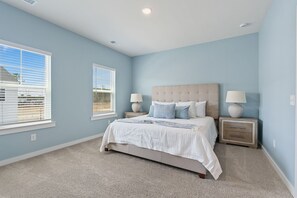 A bedroom with a bed, two bedside tables with lamps, a window with blinds, and a carpeted floor. - Cane Bay / Summerville getaway—where Southern hospitality meets modern comfort. (Summerville)