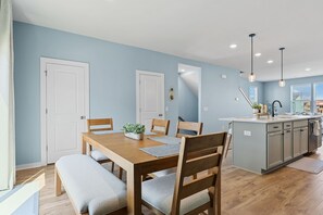 A modern kitchen with a wooden dining table, benches, and a small island with a sink. - Cane Bay / Summerville getaway—where Southern hospitality meets modern comfort. (Summerville)