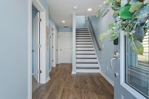 Un couloir avec un plancher en bois, un escalier et une porte sur laquelle est affiché un panneau indiquant « BIENVENUE ».