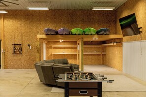 A room with a foosball table, a sofa, and a shelf with various items. - 'Riverbend Retreat' River Access! Hot Tub! Large Game Room! Kayaks! Pickle Ball! (Newport)